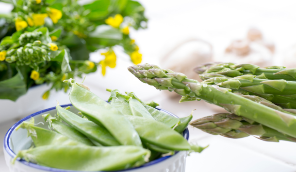 Ingredienti detox primaverili: asparagi freschi, piselli e fiori gialli su tavolo luminoso